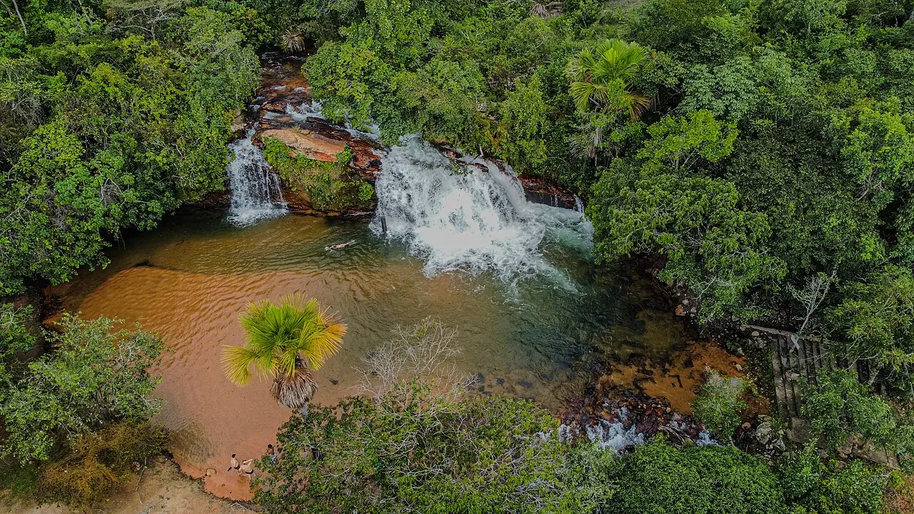 Cachoeira e poço de água clara cercados de mata, vistos de cima